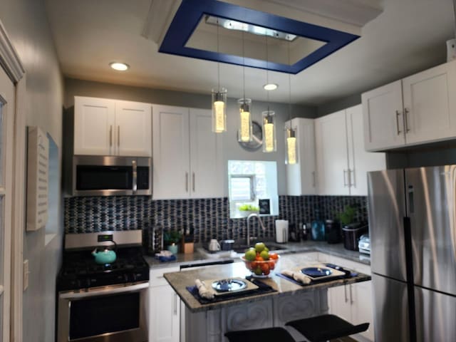 kitchen featuring stainless steel appliances, white cabinetry, hanging light fixtures, and sink