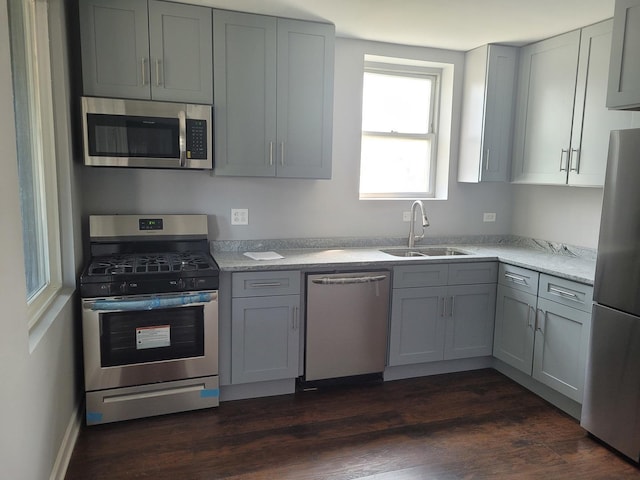 kitchen featuring gray cabinets, appliances with stainless steel finishes, dark hardwood / wood-style floors, sink, and light stone countertops