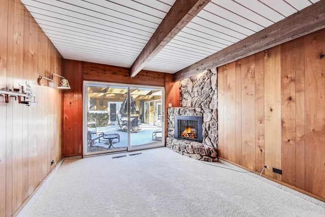 unfurnished living room with light carpet, visible vents, beamed ceiling, a stone fireplace, and wood walls