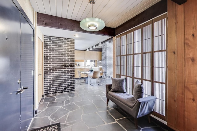 interior space featuring wood ceiling, brick wall, stone flooring, and beamed ceiling