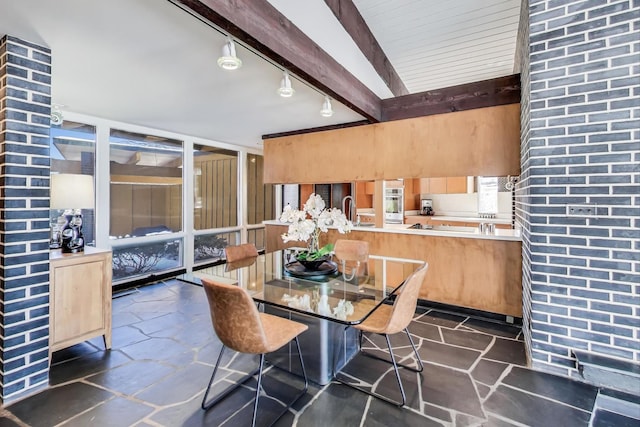 dining area featuring stone tile flooring, rail lighting, expansive windows, and beamed ceiling