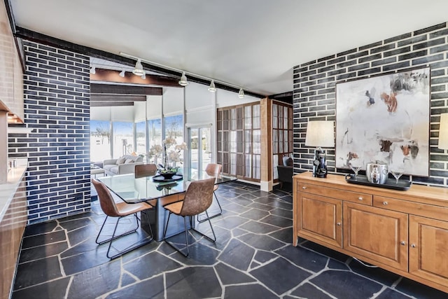 dining room featuring stone tile flooring, rail lighting, and brick wall