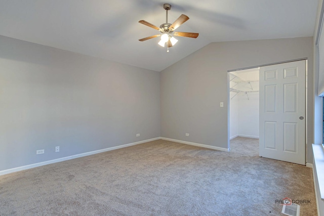 unfurnished bedroom featuring lofted ceiling, a walk in closet, light colored carpet, ceiling fan, and a closet