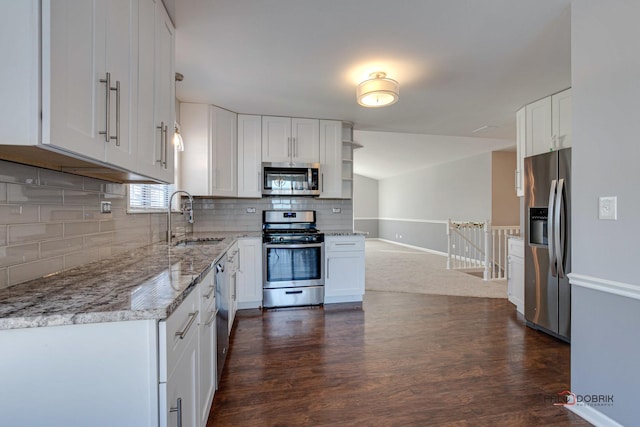 kitchen with appliances with stainless steel finishes, white cabinetry, sink, decorative backsplash, and light stone countertops