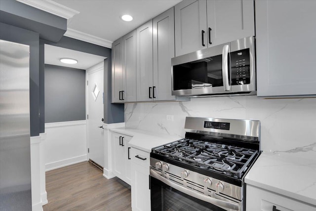 kitchen featuring wood-type flooring, ornamental molding, stainless steel appliances, light stone countertops, and decorative backsplash