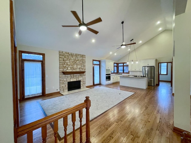 unfurnished living room with a stone fireplace, high vaulted ceiling, sink, ceiling fan, and light hardwood / wood-style floors