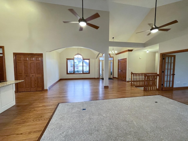 unfurnished living room with hardwood / wood-style flooring, ceiling fan with notable chandelier, and high vaulted ceiling