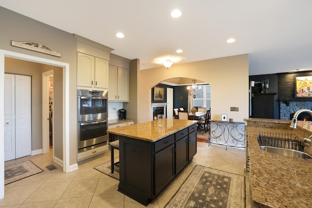 kitchen featuring double oven, a center island, a sink, and a lit fireplace