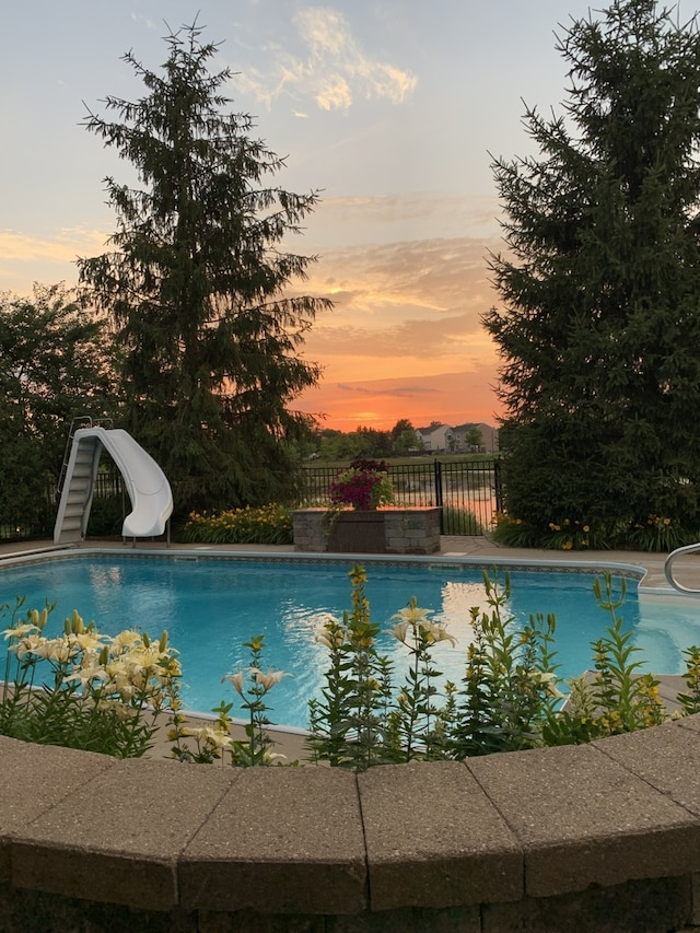 pool at dusk featuring fence, an outdoor pool, and a water slide