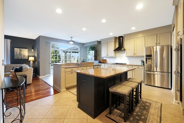 kitchen with wall chimney exhaust hood, a kitchen island, appliances with stainless steel finishes, and light tile patterned flooring