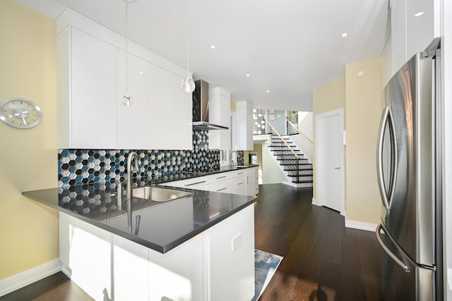 kitchen with wall chimney range hood, white cabinets, stainless steel refrigerator, and kitchen peninsula