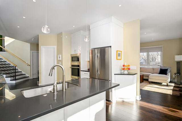 kitchen with appliances with stainless steel finishes, sink, white cabinets, hanging light fixtures, and dark wood-type flooring