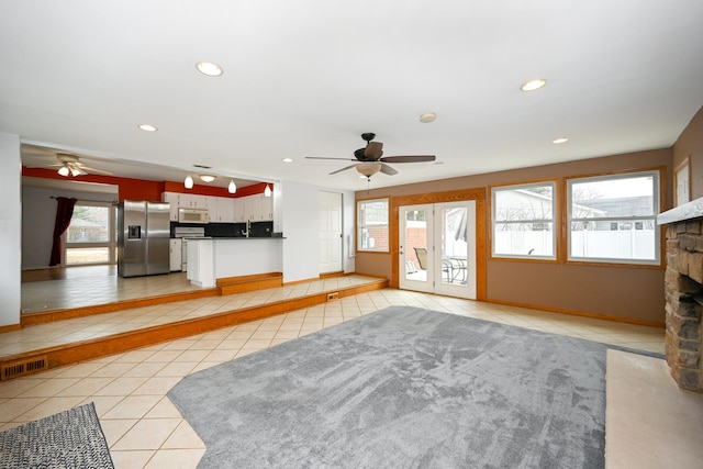 unfurnished living room featuring sink, a stone fireplace, ceiling fan, and light tile patterned flooring