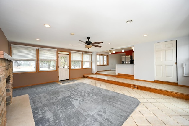 unfurnished living room featuring light tile patterned flooring, a stone fireplace, and ceiling fan