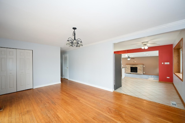 interior space featuring ornamental molding, a fireplace, ceiling fan with notable chandelier, and light hardwood / wood-style flooring