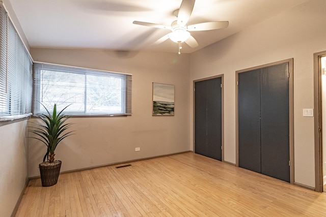 unfurnished bedroom with ceiling fan, two closets, vaulted ceiling, and light wood-type flooring