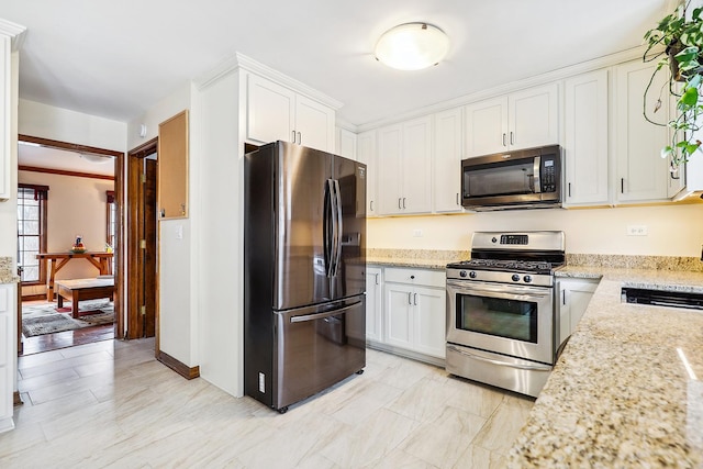 kitchen featuring white cabinetry, light stone countertops, crown molding, and stainless steel appliances