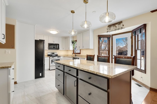 kitchen with stainless steel gas range oven, white cabinetry, refrigerator, a kitchen island, and pendant lighting