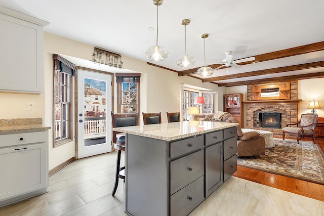 kitchen featuring a breakfast bar, white cabinetry, light stone counters, pendant lighting, and a fireplace