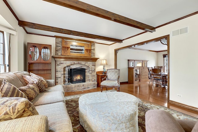 living room featuring beamed ceiling, crown molding, a brick fireplace, and hardwood / wood-style floors