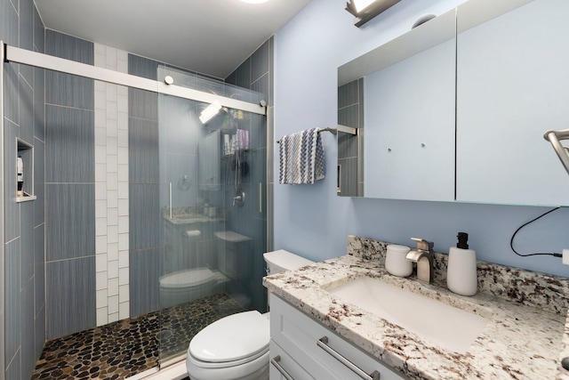 bathroom featuring vanity, a shower with shower door, and toilet