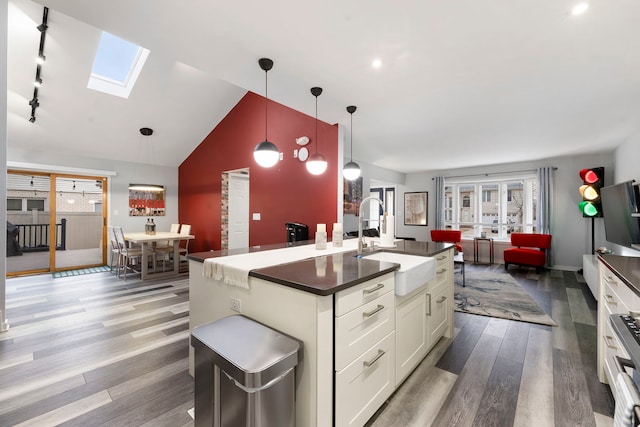 kitchen featuring lofted ceiling with skylight, sink, decorative light fixtures, hardwood / wood-style floors, and white cabinets