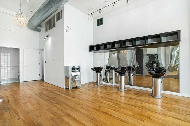 interior space with wood-type flooring, rail lighting, a high ceiling, and a notable chandelier