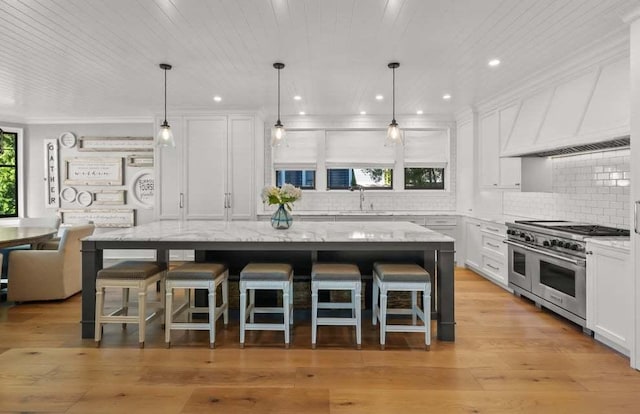 kitchen featuring white cabinetry, light stone counters, a kitchen breakfast bar, a kitchen island, and range with two ovens