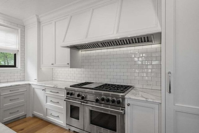 kitchen with white cabinetry, backsplash, range with two ovens, light hardwood / wood-style floors, and light stone countertops