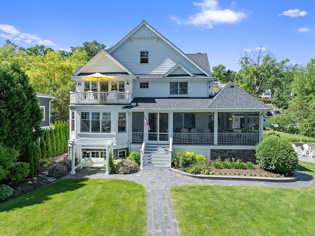 rear view of house with a lawn, a sunroom, and a balcony