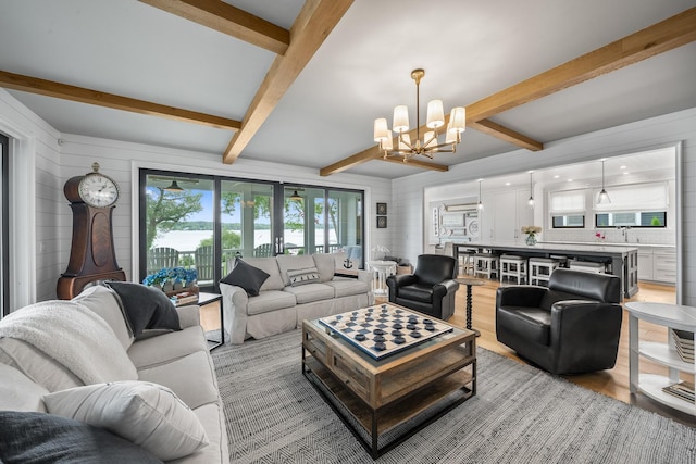 living room featuring beam ceiling, light hardwood / wood-style floors, and a notable chandelier