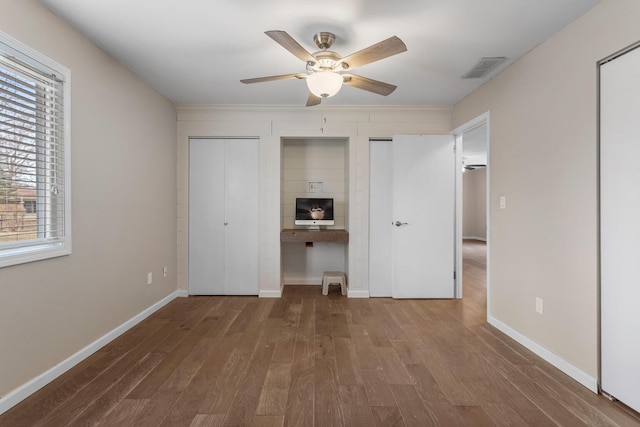 unfurnished bedroom with wood finished floors, visible vents, baseboards, and two closets