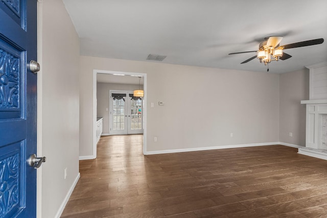 unfurnished living room featuring dark wood-style floors, a fireplace with raised hearth, visible vents, a ceiling fan, and baseboards