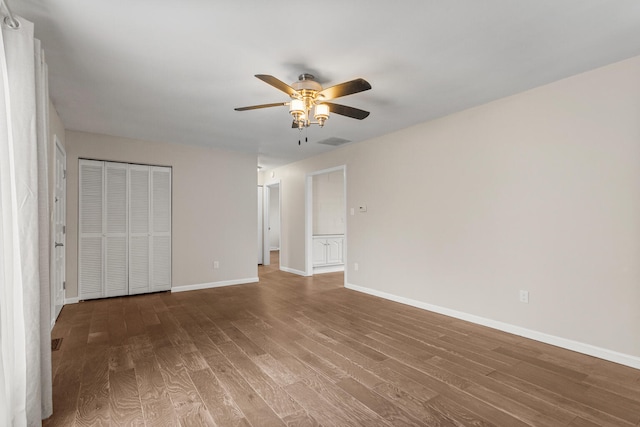 unfurnished bedroom featuring ceiling fan, wood finished floors, visible vents, baseboards, and a closet