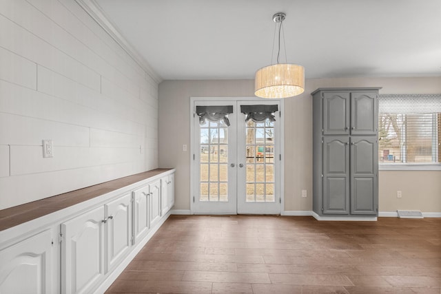 unfurnished dining area featuring baseboards, visible vents, wood finished floors, crown molding, and french doors