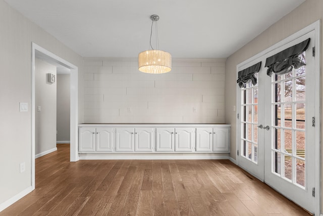 unfurnished dining area featuring light wood-style floors, visible vents, baseboards, and french doors