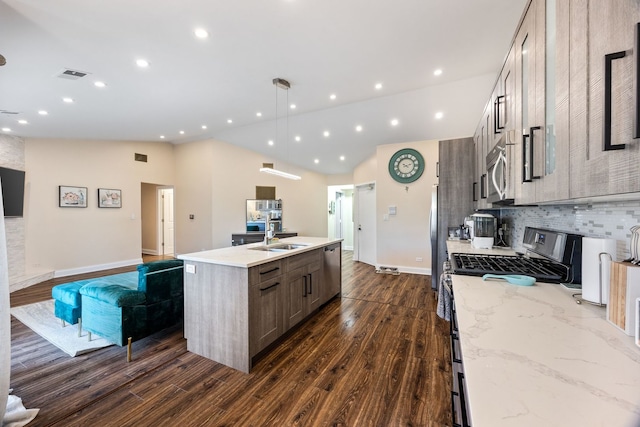 kitchen featuring dark wood-type flooring, lofted ceiling, appliances with stainless steel finishes, pendant lighting, and light stone countertops