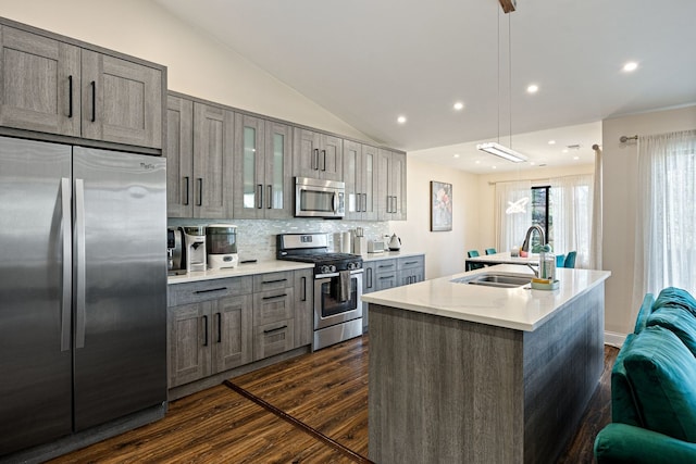 kitchen featuring vaulted ceiling, appliances with stainless steel finishes, an island with sink, sink, and dark wood-type flooring