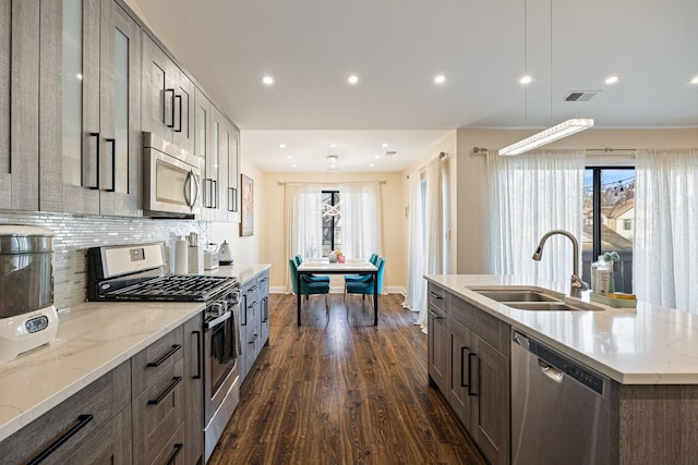 kitchen with sink, a center island with sink, dark hardwood / wood-style flooring, stainless steel appliances, and decorative backsplash