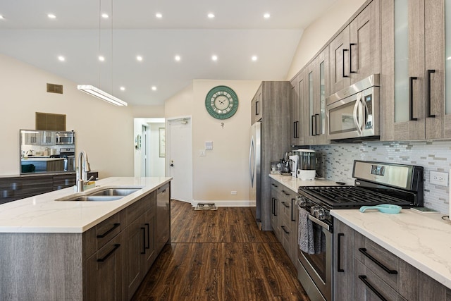 kitchen with vaulted ceiling, appliances with stainless steel finishes, sink, a kitchen island with sink, and dark wood-type flooring