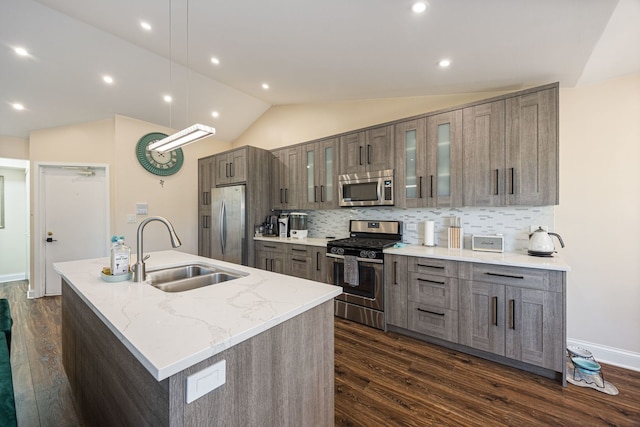 kitchen with sink, appliances with stainless steel finishes, light stone countertops, a center island with sink, and decorative light fixtures