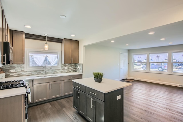 kitchen with sink, gas range, dark hardwood / wood-style floors, a kitchen island, and pendant lighting