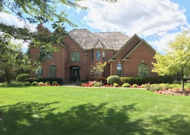 view of front of home featuring a front yard, brick siding, and a chimney