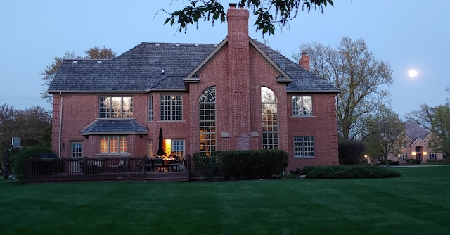 rear view of house with brick siding, a lawn, a chimney, and a deck