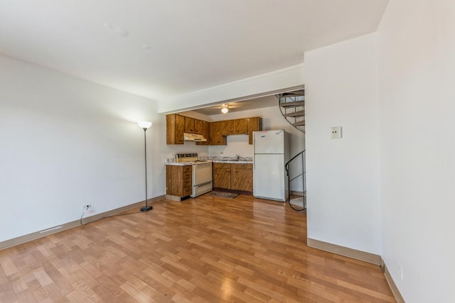 kitchen featuring brown cabinets, light countertops, light wood-style flooring, white appliances, and under cabinet range hood