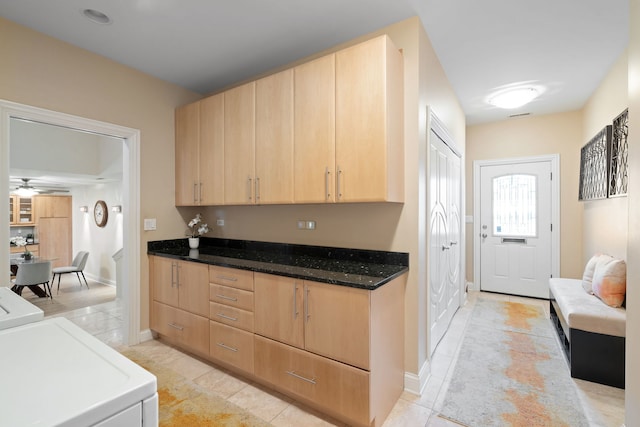 kitchen with light brown cabinetry, separate washer and dryer, dark stone countertops, light tile patterned floors, and ceiling fan