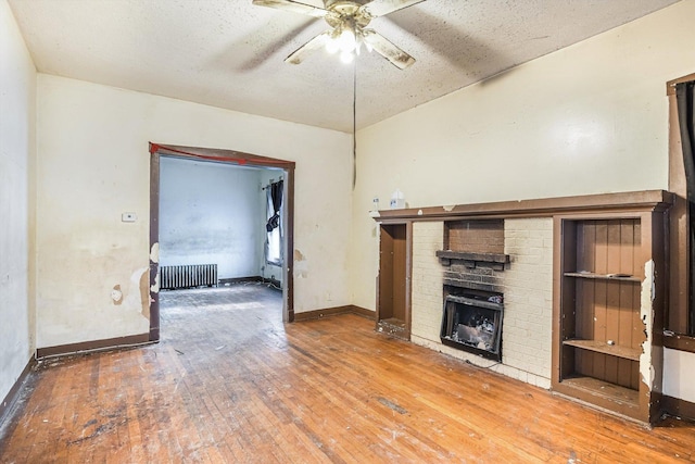 unfurnished living room with a fireplace, radiator heating unit, hardwood / wood-style floors, and ceiling fan