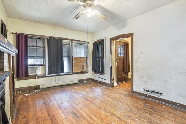 empty room featuring cooling unit, ceiling fan, hardwood / wood-style floors, and a textured ceiling