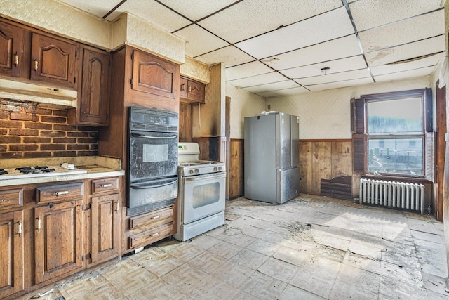 kitchen with white appliances, radiator heating unit, wooden walls, and a paneled ceiling