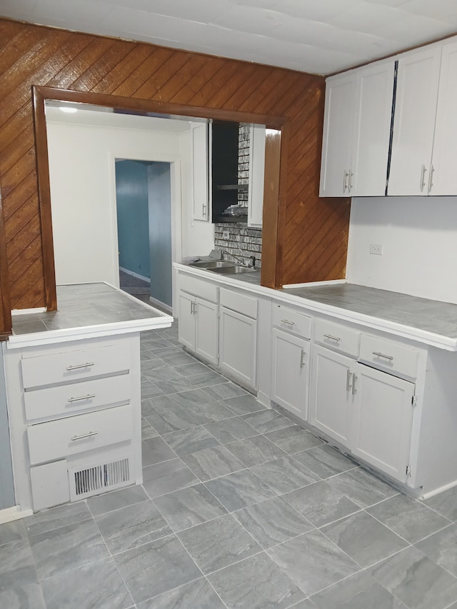 kitchen with sink, backsplash, white cabinets, and wooden walls